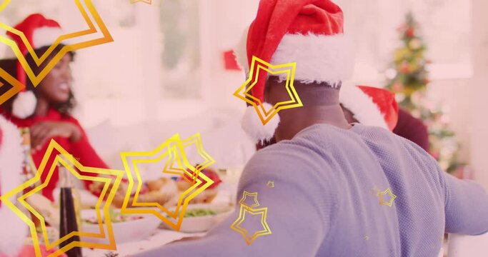 Animation of stars falling over happy african american family wearing santa hats and having dinner