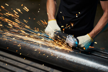 angle grinder for grinding metal in male hands grinds metal pipe with sparks - obrazy, fototapety, plakaty