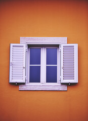 white window with shutters on a yellow house