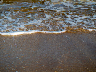 Wave with white foamy coastline beach. Sandy shore.