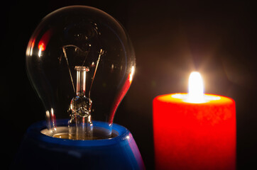 A switched off light bulb illuminated by the light of a burning candle in complete darkness....