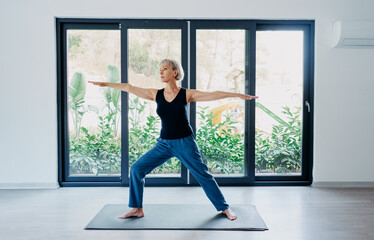 Fototapeta premium Yoga at home. Senior woman exercising indoor. Concept of healthy lifestyle.