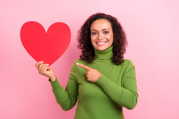 Photo of sweet charming african lady dressed green turtleneck smiling pointing finger large paper heart isolated pink color background