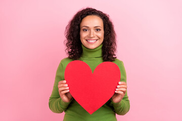 Photo of adorable dreamy afro woman wear green turtleneck holding big red heart smiling isolated pink color background