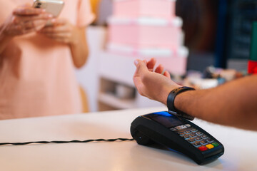 Close-up view of unrecognizable man paying with NFC technology smart watch contactless on POS terminal, selective focus, blurred background. Contactless payment using modern technology.