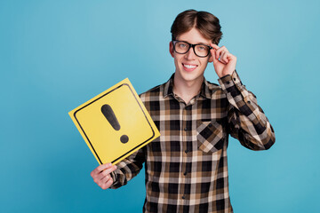Photo of young guy hold paper card sign attention warning symbol isolated over blue color background
