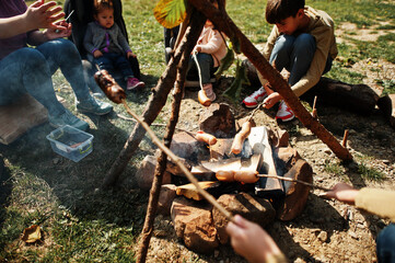 Family bonfire in mountain. Frying sausages. Mother with four kids camping. Autumn hike and camp weather. Warming and cooking near flame together.