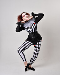Full length  portrait of red haired  girl wearing a black and white clown jester costume,...