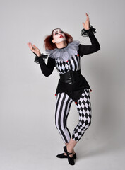 Full length  portrait of red haired  girl wearing a black and white clown jester costume, theatrical circus character.  Standing pose  isolated on  studio background.