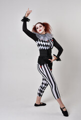 Full length  portrait of red haired  girl wearing a black and white clown jester costume, theatrical circus character.  Standing pose  isolated on  studio background.