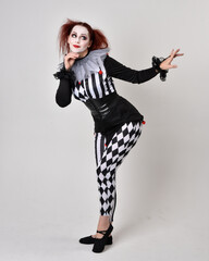 Full length  portrait of red haired  girl wearing a black and white clown jester costume,...