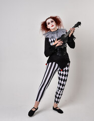 Full length  portrait of red haired  girl wearing a black and white clown jester costume, theatrical circus character.  Standing pose  isolated on  studio background.