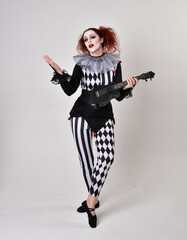 Full length  portrait of red haired  girl wearing a black and white clown jester costume, theatrical circus character.  Standing pose  isolated on  studio background.