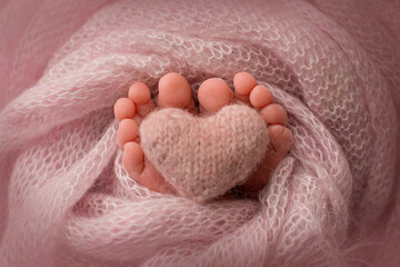 Legs, toes, feet and heels of a newborn. Wrapped in a pink knitted blanket. Knitted heart in baby's legs. 