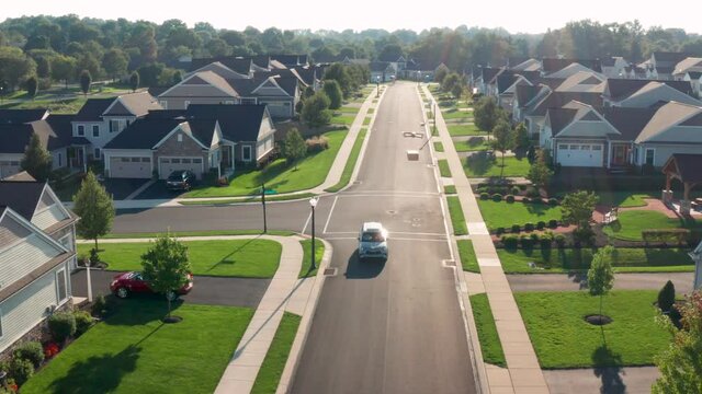 Drone delivers package to homes in residential community. Car turns on street. Aerial of UAV.