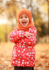 Portrait of a beautiful girl in an orange hat and a scarf, the child smiles, a walk in the autumn park.
