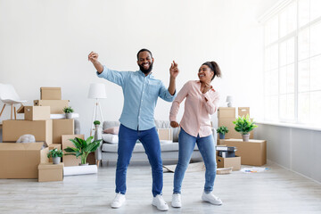 Fototapeta na wymiar Satisfies excited young african american lady and guy dancing in living room with cardboard boxes with things