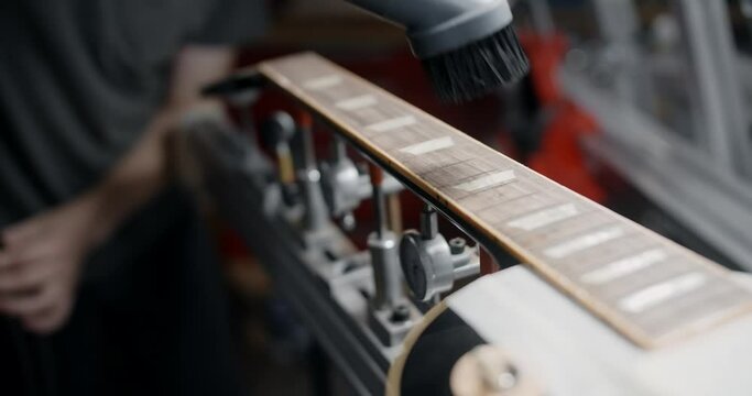 Guitar tech uses vacuum cleaner the to remove the wood dust from guitar neck after sanding, musical instruments repair shop, 4k 60fps 10 bit