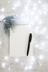 a notebook in a Christmas garland with a branch of a fir tree in silver color, a black pen. light background