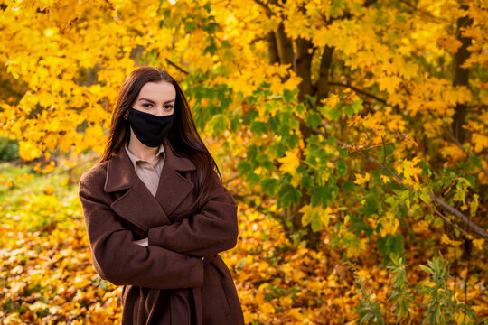 Portrait of a young woman with black mouth mask in a brown coat in autumn