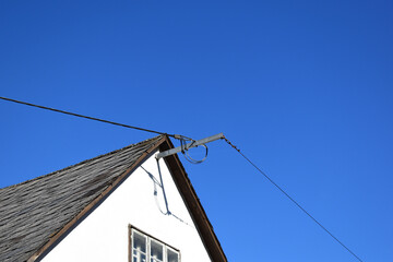 Oberirdische Stromversorgung mit Stromkabel beim Eintritt unter dem Hausdach vor blauem Himmel, weißes Haus mit grauen Dachschindeln