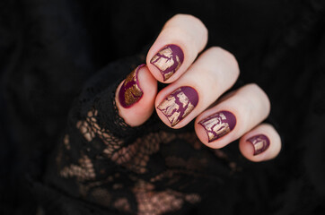 Burgundy golg cracle matte nail polish. Manicured nail with dark matte nail polish isolated on black.