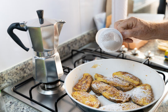 Hand Of Senior Man Pouring Powdered Sugar On French Toasts In Pan By Italian Coffee Maker On Kitchen Stove