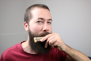 Young bearded caucasian man playing harmonica 