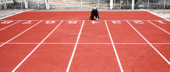 Obraz premium Athletic woman in sport clothes on starting line prepares to run at the running on athletic track. Female runner ready for sports exercise.
