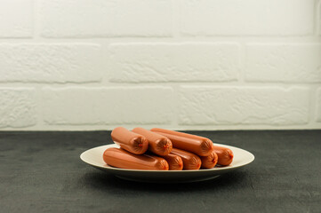 fresh diet sausages on a ceramic plate on a black countertop against a white brick wall.
