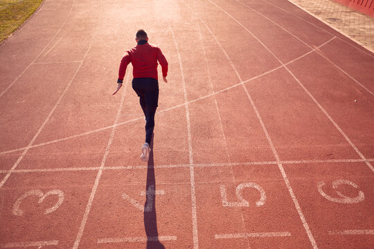 Young Adult Male Athlete From Behind Started Run From  The Start Position Number Four  At Athletic Track.