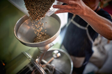 A man is making ground coffee by pouring beans into the grinder. Coffee, beverage, producing