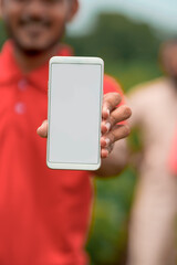 Young indian agronomist or banker showing smartphone with farmers at agriculture field.