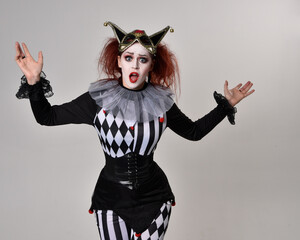 close up portrait of red haired  girl wearing a black and white clown jester costume, theatrical circus character.  Standing pose  isolated on  studio background.