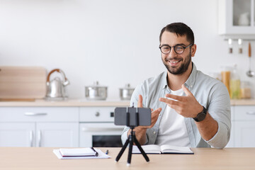 Cheerful adult european male teacher with beard in glasses gesturing and look at phone webcam