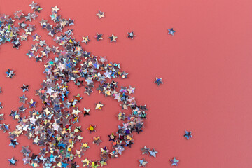 Glitter stars confetti on pink background in bright pastel colors. Festive Christmas background. Festive holiday pastel backdrop
