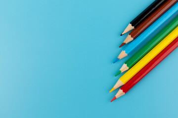 Six colored pencils close-up on a blue background with a copy of the space. The texture of bright colored wooden pencils.