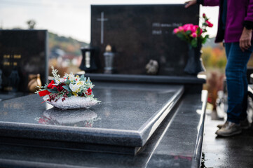 Bouquet of colorful flowers on a grave, with an unrecognizable woman paying some respect in blurred background