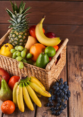 Mix of fresh juicy colorful exotic tropical fruits in basket on wooden background