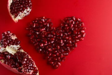 Heart shaped juicy ruby pomegranate seeds isolated on red background, love garnet, valentine's day...