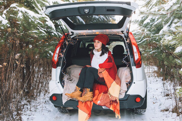 smiling pretty woman in car trunk at snowed winter forest