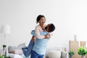Happy couple moving at bought house, husband lifts up beloved wife, family begin new life at first dwelling