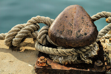 Fototapeta na wymiar Rusty mooring bollard with tied rope in the port