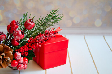 red gift box and a branch of a christmas tree on a golden bokeh background. New year gift and decor close up with space for text