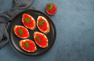Fresh sandwiches with red caviar, butter and parsley on a graphite background. Top view, copy space.