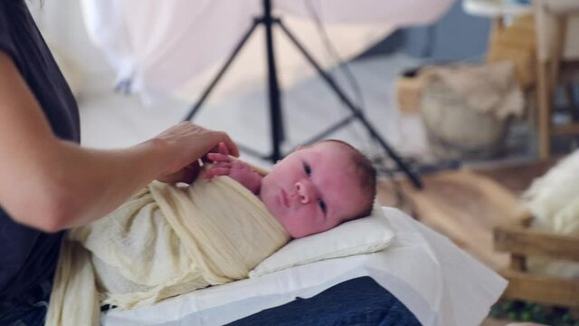 A tiny baby is swaddled before photographing. Professional photography of a baby in the studio, behind the scenes. A newborn baby is being prepared for photography