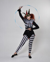Full length  portrait of red haired  girl wearing a black and white clown jester costume, theatrical circus character.  Standing pose with hula hoop, isolated on  studio background.
 - obrazy, fototapety, plakaty