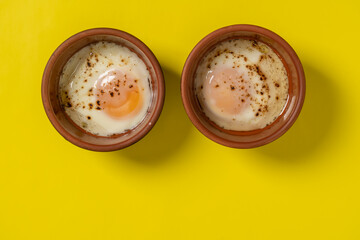 Two fried eggs in a round ceramic dish in the form of eyes on yellow background. Cooked small fried eggs is a simple breakfast