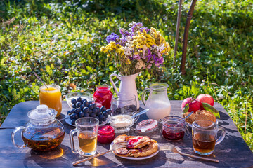 Tea, pancakes, milk and jam on the breakfast table in the autumn garden, close up
