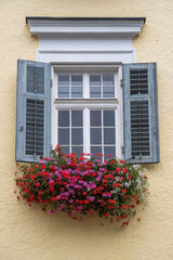 Beige plaster facade of a mountain house and windows with colorful flowers in Austria